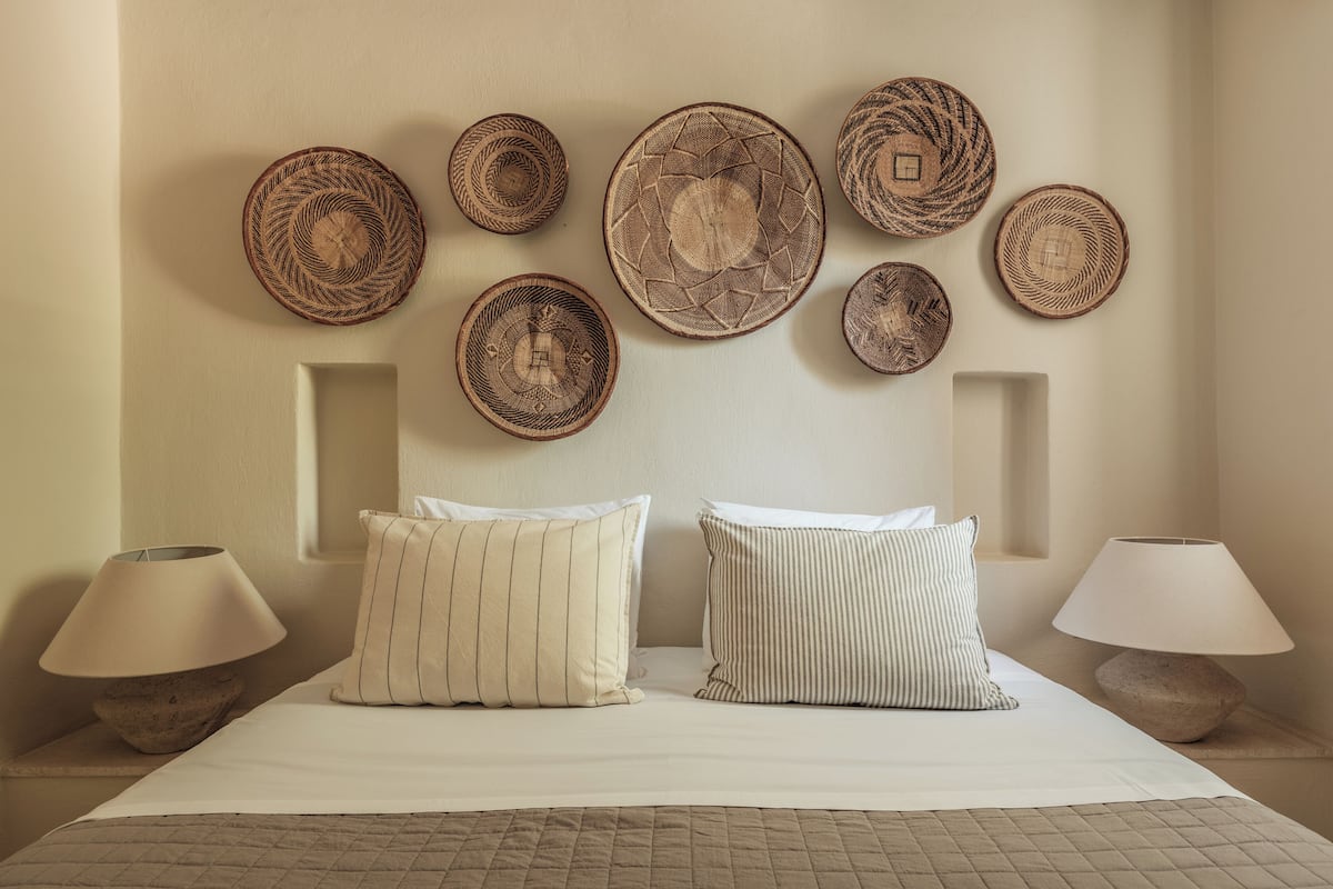 Un dormitorio con una cama, dos almohadas, dos lámparas de noche y un muro decorado con cestas tejidas.