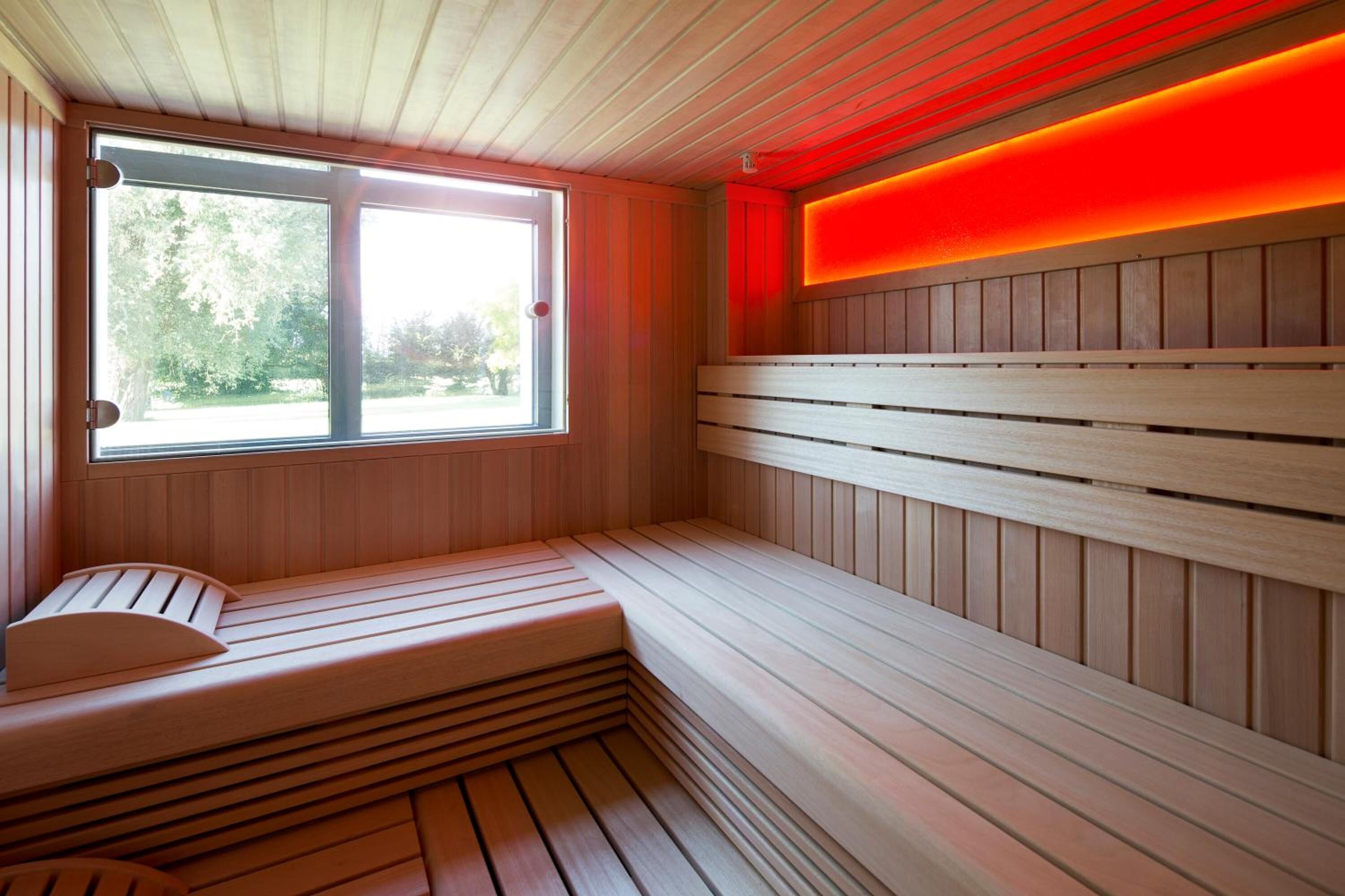 A sauna with wooden benches, a window, and a red-lit wall.