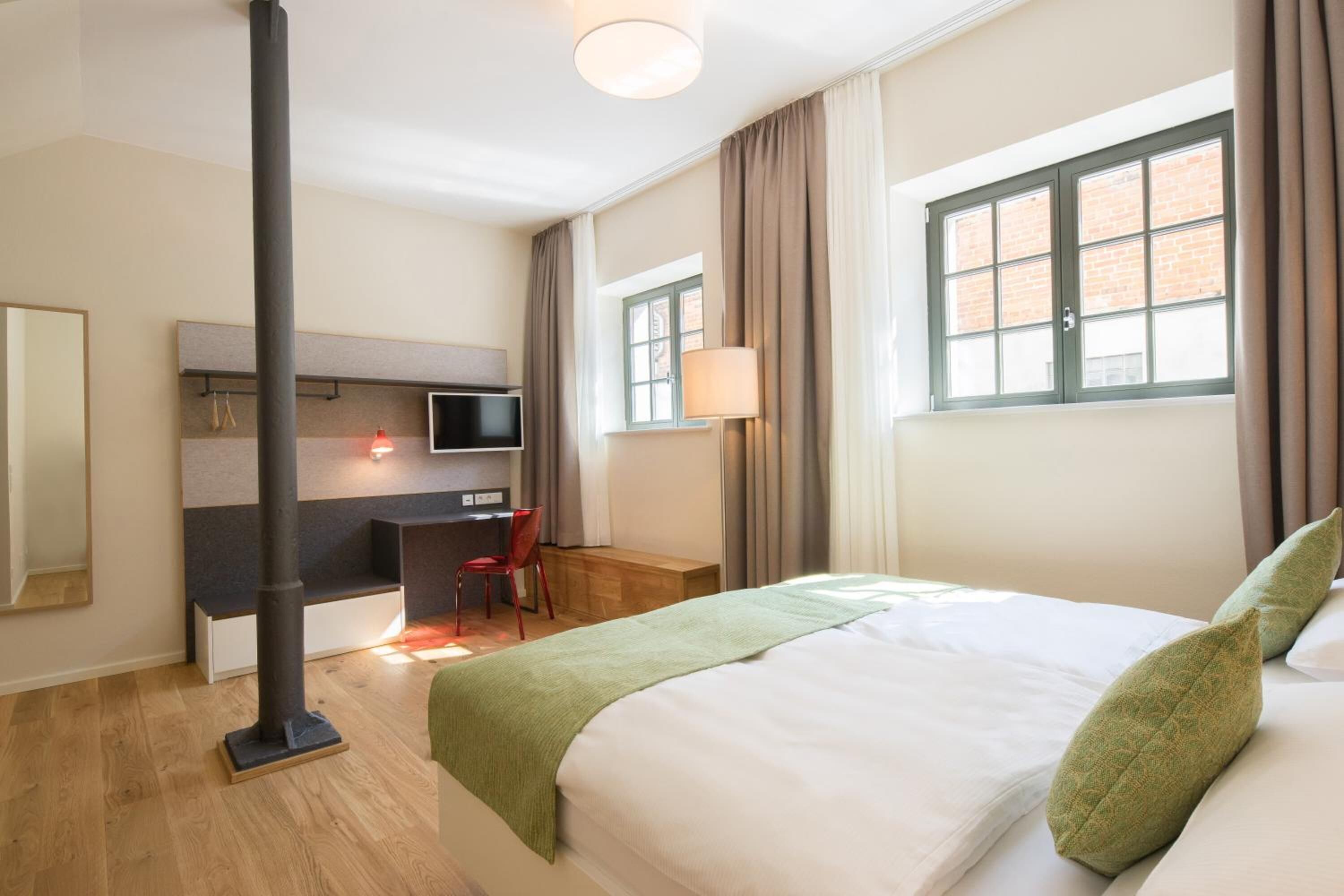 Une chambre d’hôtel équipée d’un lit, d’un bureau, d’une chaise, d’une télévision et d’une fenêtre avec des rideaux.