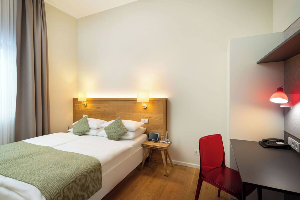 Una habitación de hotel con cama, mesita de noche, lámpara, silla y escritorio.