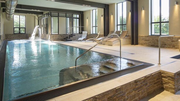 Ein überdachter Pool mit Wasserfall, Steinwänden und großen Fenstern.