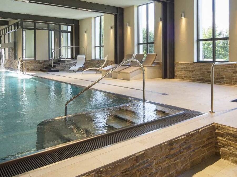 An indoor swimming pool with a waterfall feature, stone walls, and large windows.
