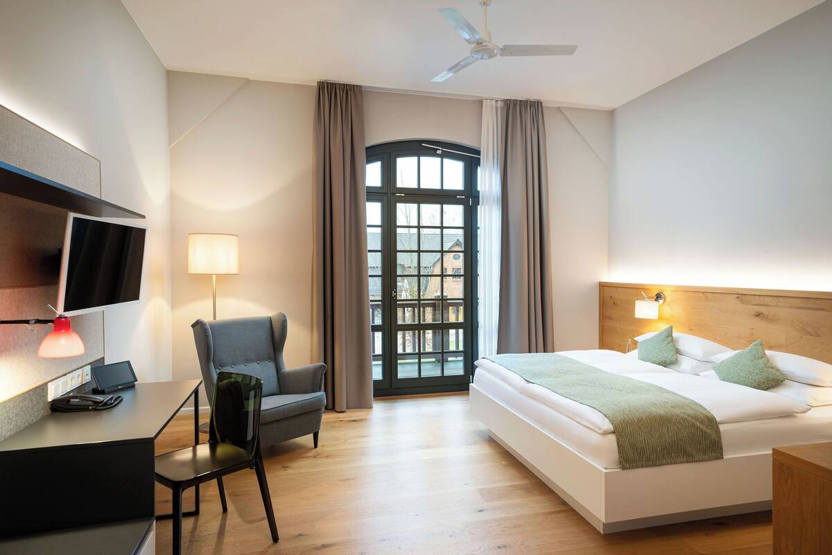 Una habitación de hotel moderna con cama, escritorio, silla y un ventanal con cortinas.