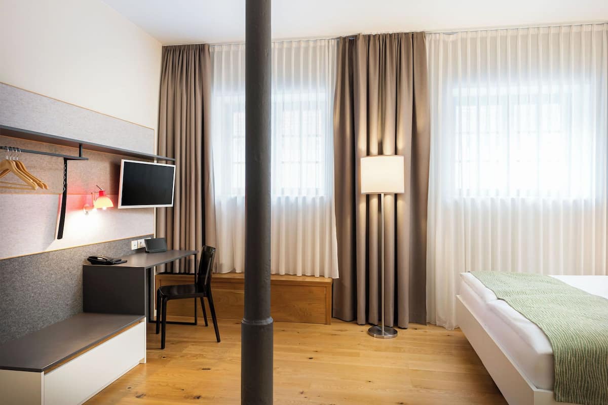Habitación de hotel con cama, escritorio con computadora, silla, televisión y lámpara.