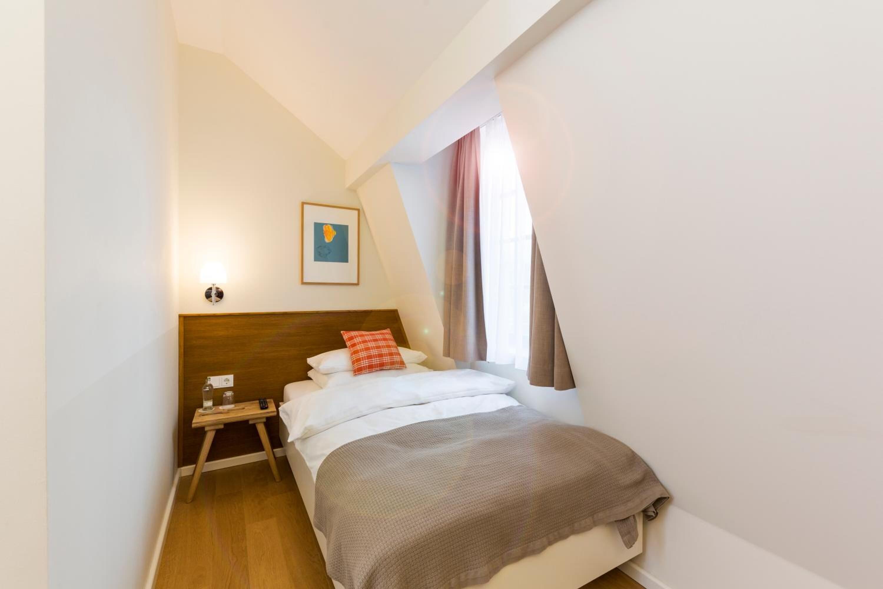 A bedroom with a bed, a nightstand, a framed picture, and a window with curtains.