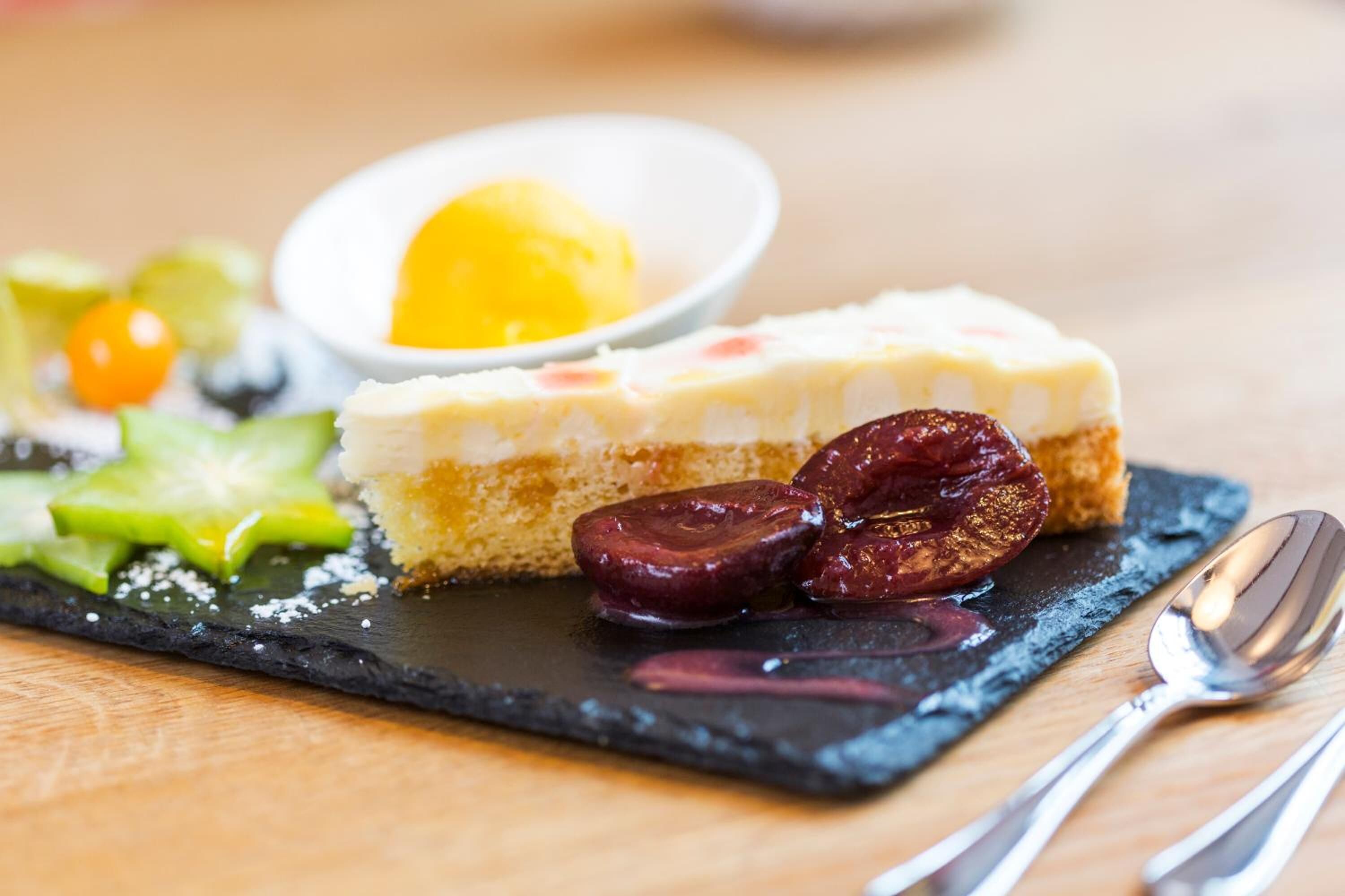A dessert plate with a slice of cheesecake, a scoop of ice cream, and some fruit on a slate board.