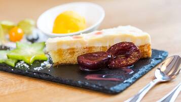 A dessert plate with a slice of cheesecake, a scoop of ice cream, and some fruit on a slate board.