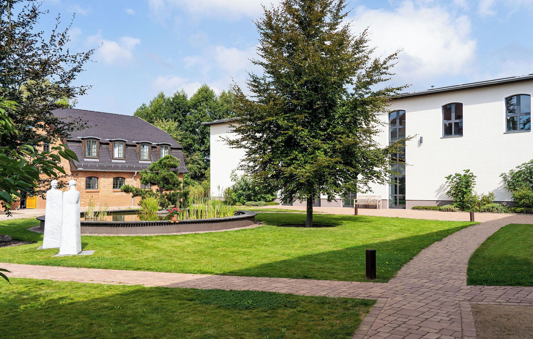 A courtyard with a brick pathway, a white building, and a tree.