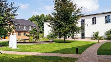 A courtyard with a brick pathway, a white building, and a tree.