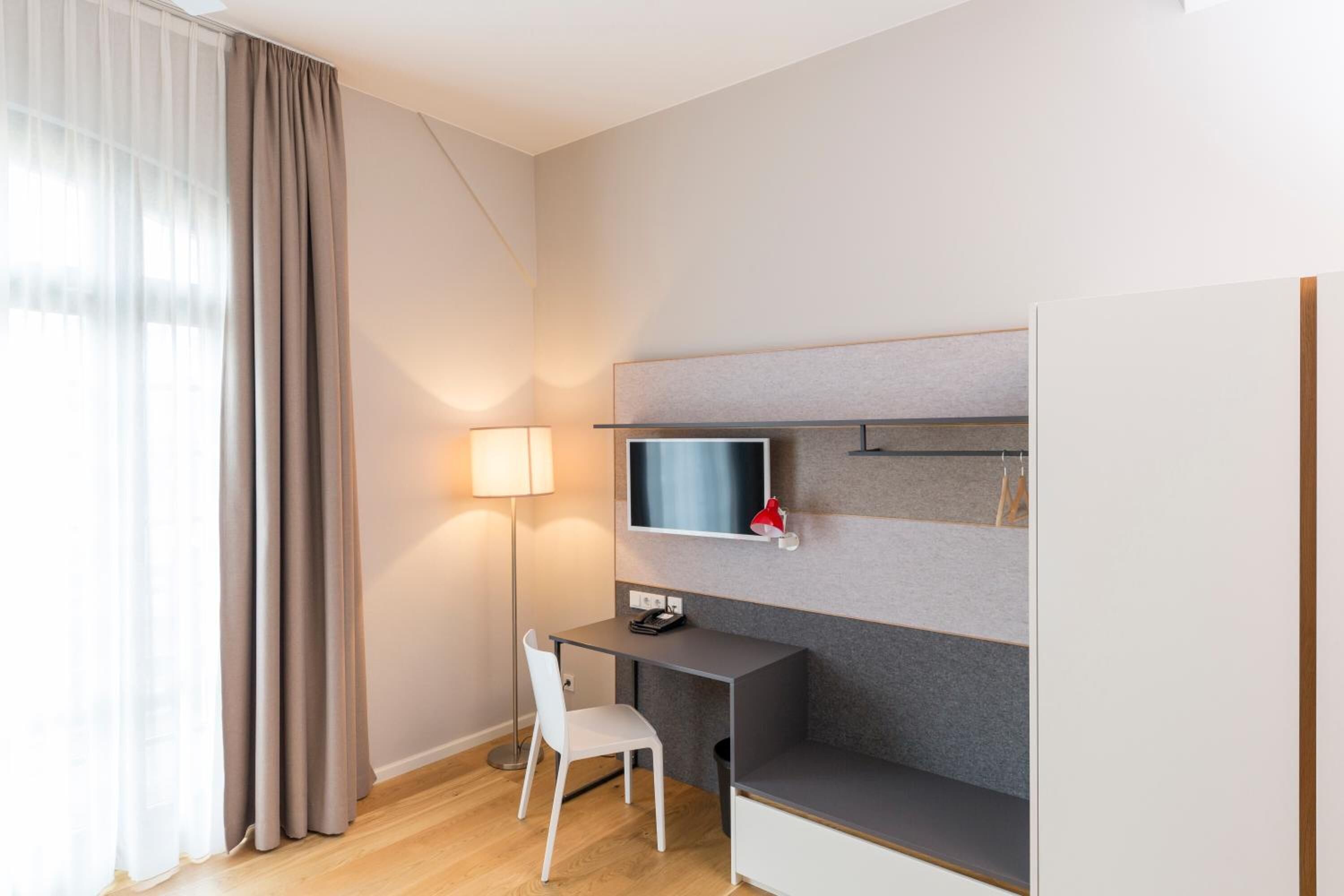 A modern hotel room with a desk, chair, and a mounted TV.