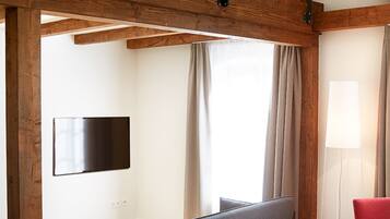 A hotel room with a wooden ceiling, a flat-screen TV mounted on the wall, a bed with white bedding, and a red chair.