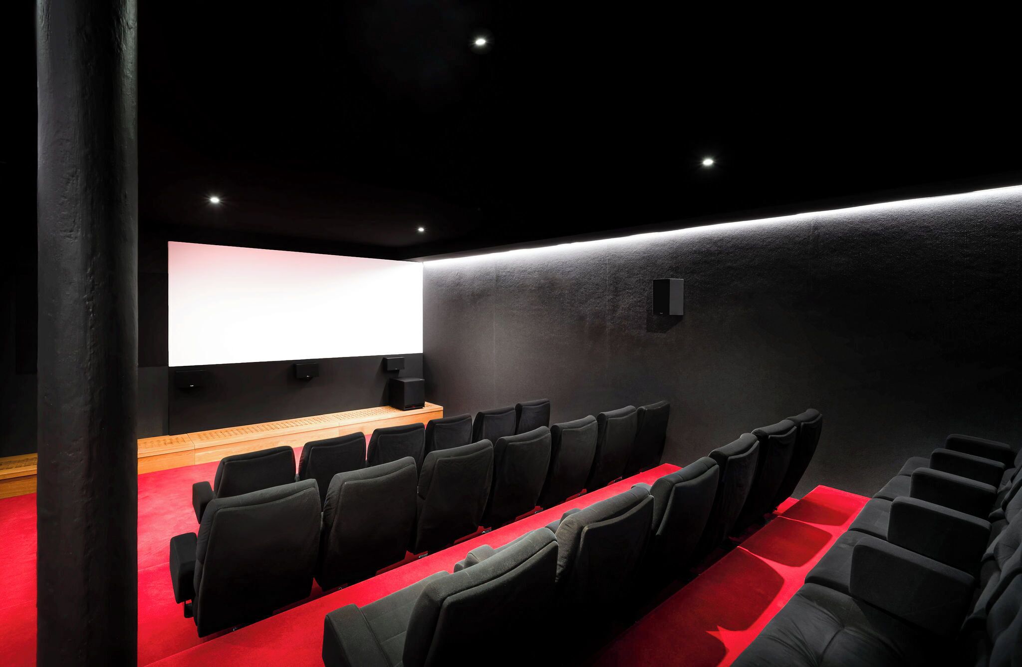 Una sala de cine moderna con filas de asientos negros, una pantalla grande y un mostrador de madera.