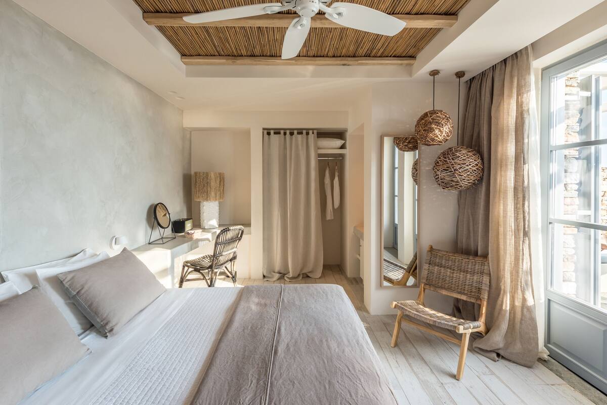 Un dormitorio con cama, escritorio, silla, armario y un gran ventanal con cortinas.