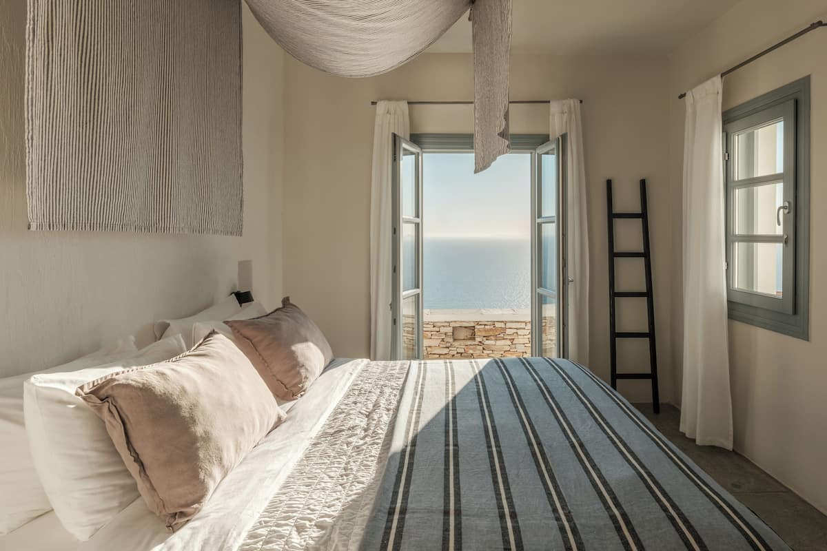 Un dormitorio con cama, vista al mar a través de una puerta abierta, una escalera y una lámpara colgante.
