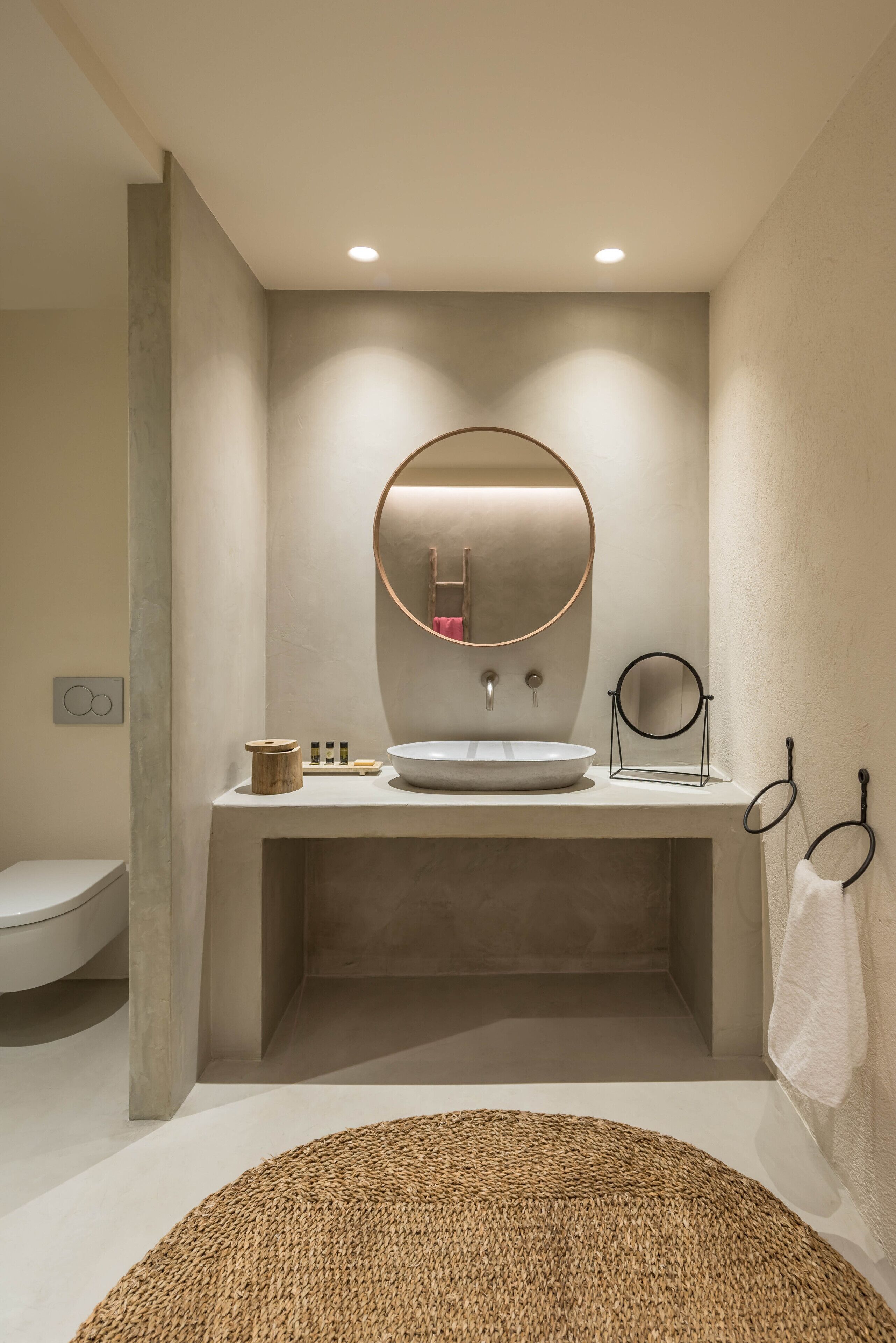 Un baño moderno con un espejo redondo, un lavamanos y un perchero para toallas.