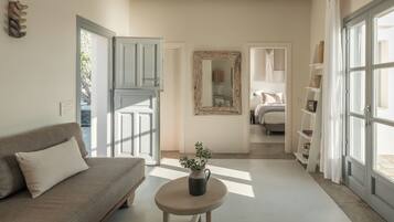 Una habitación con un sofá, una mesita redonda con una planta, un espejo y una cama al fondo.