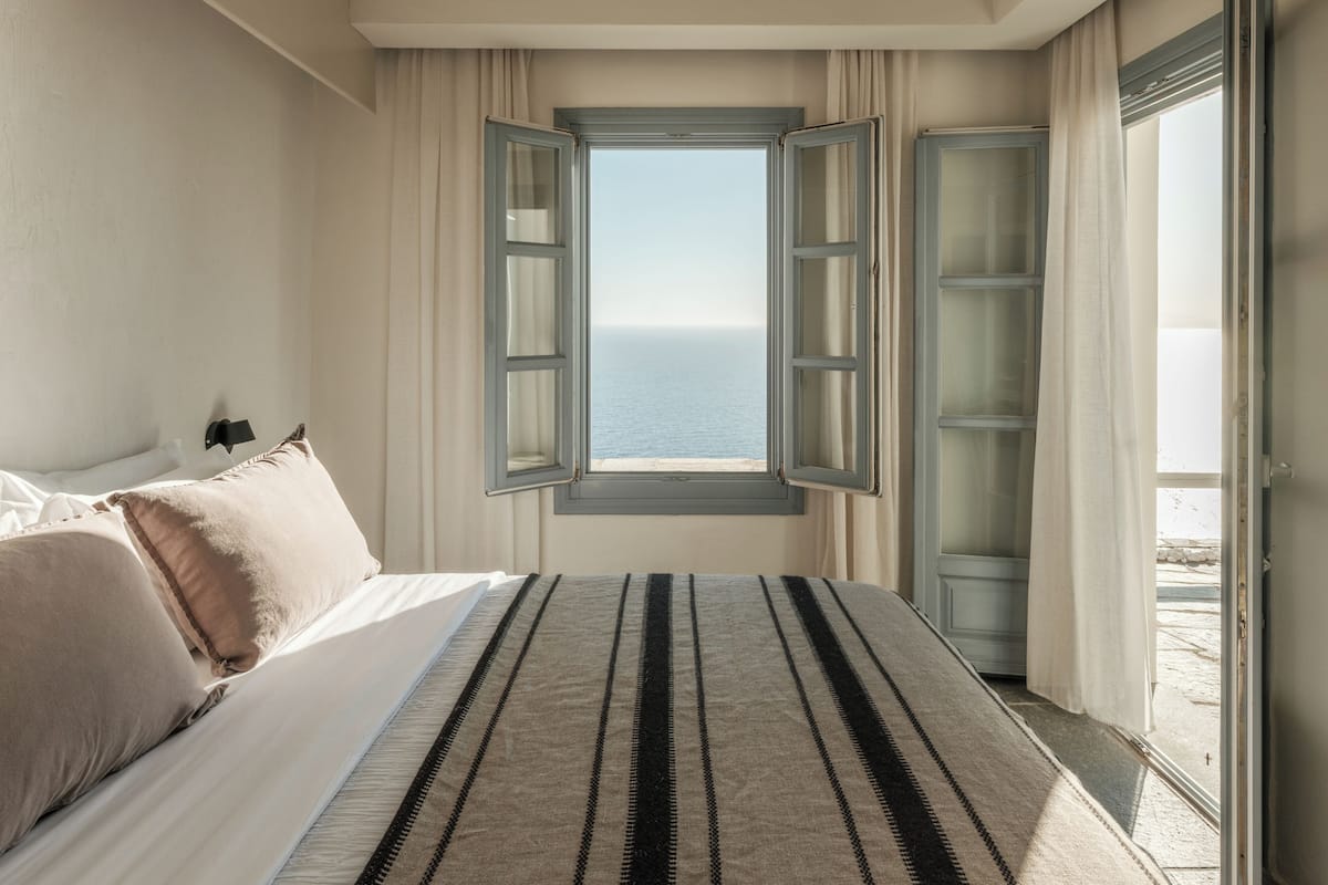 Un dormitorio con cama, ventana con cortinas y vista al mar.