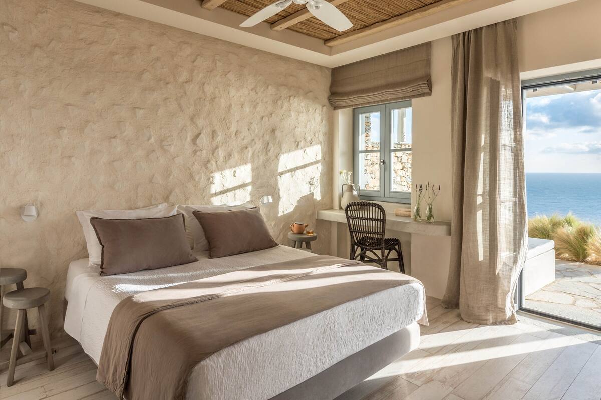 Un dormitorio con una cama grande, una mesita, una silla y vistas al mar.