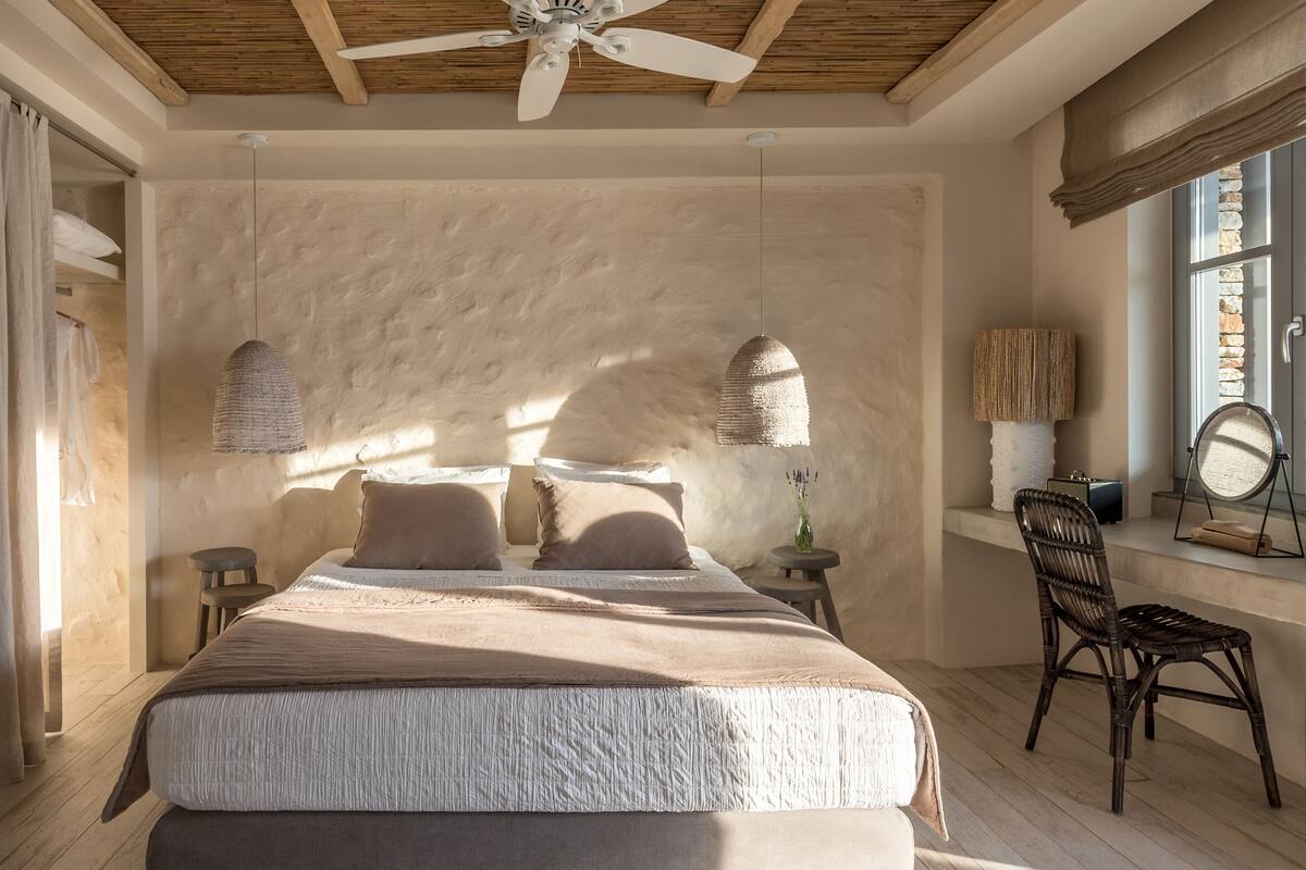 Un dormitorio con una cama grande, un ventilador de techo, una ventana con vistas y una mesita de noche con lámpara.
