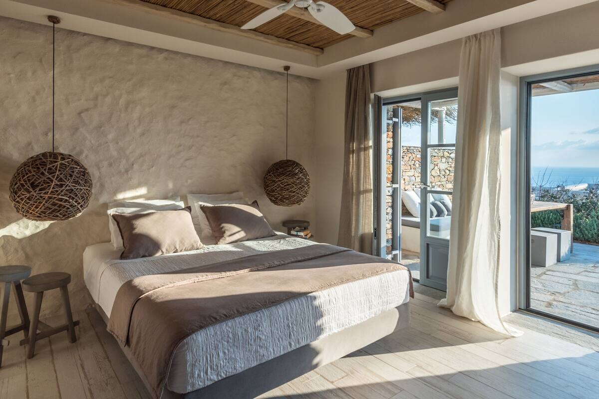 Un dormitorio con una cama grande, un ventilador de techo y vista al mar a través de un ventanal.