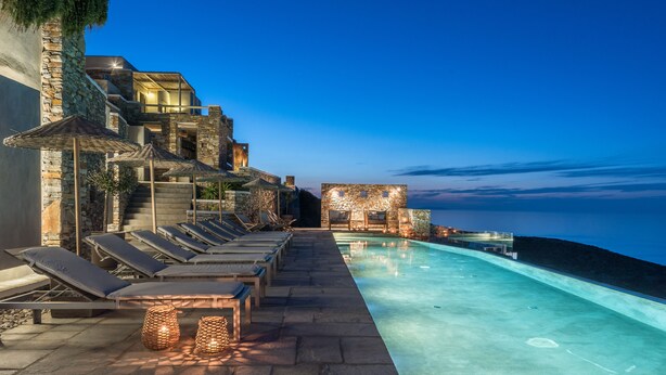 A luxurious poolside area with lounge chairs and a stone wall, overlooking a body of water.