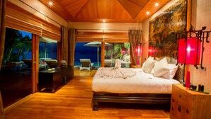 Un dormitorio amplio con una cama grande, piso de madera y vista al océano por la noche.