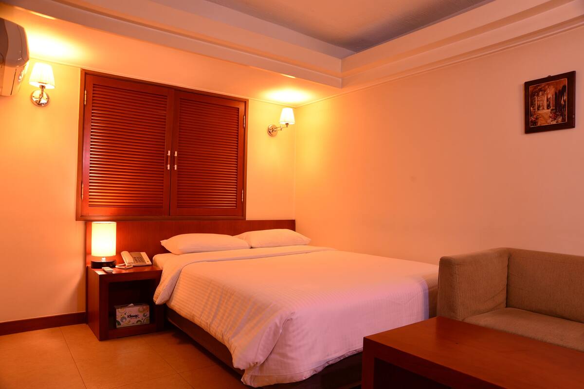 A hotel room with a bed, bedside table with a lamp, a couch, and a wall-mounted picture.