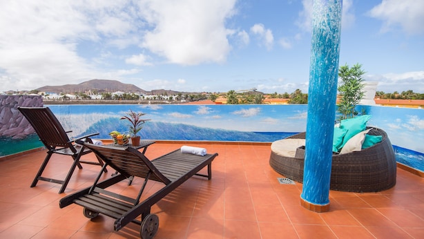 Una terraza iluminada por el sol con piscina, sillones de descanso y un sofá de mimbre.