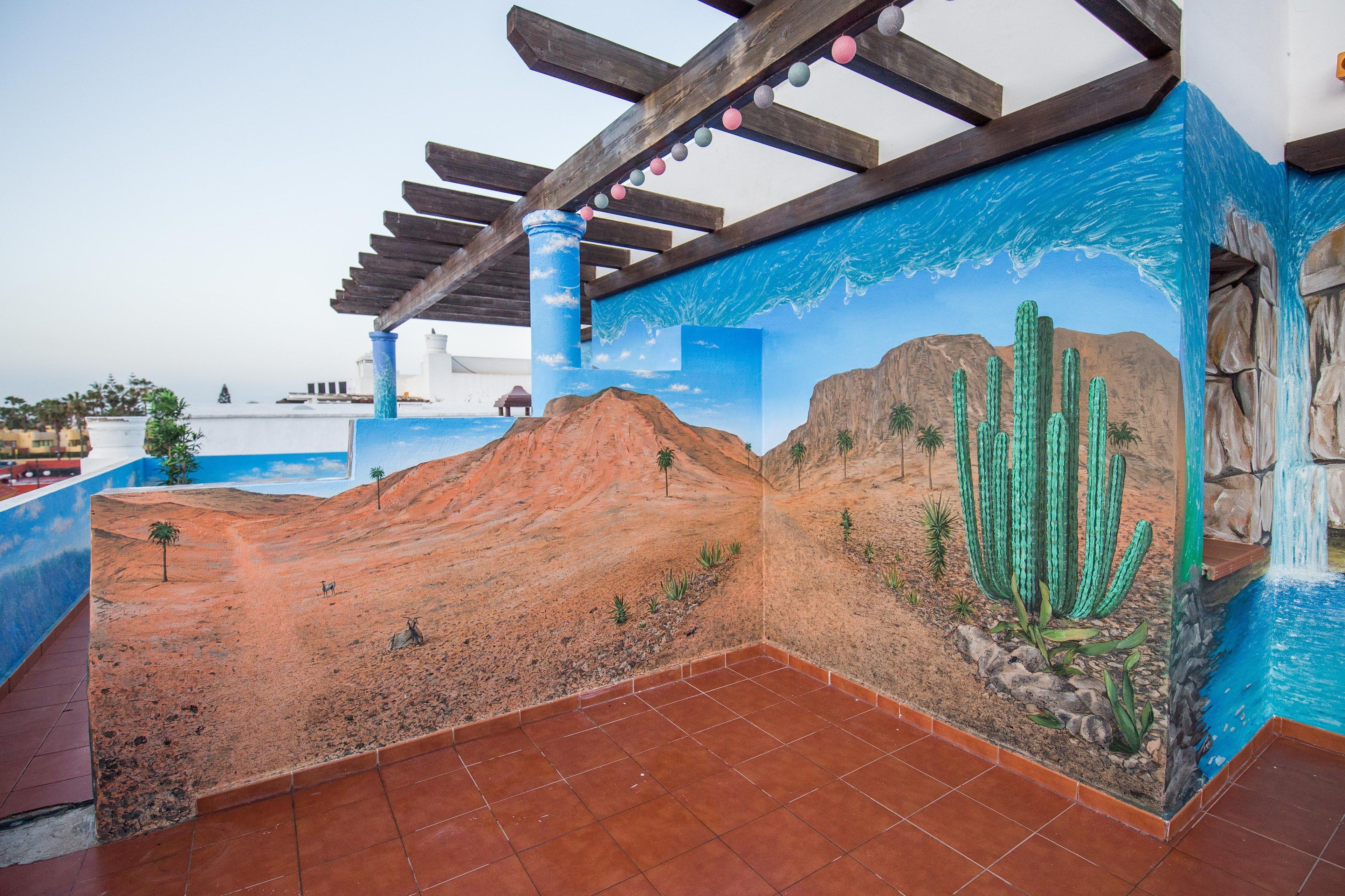 A room with a mural of a desert landscape, a wooden ceiling structure, and a tiled floor.