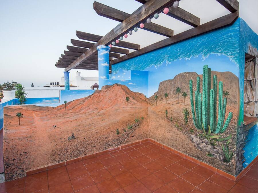 Una habitación con un mural de un paisaje desértico, estructura de techo de madera y piso de baldosas.