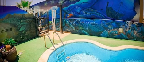 A swimming pool with a mural depicting underwater scenes, surrounded by a white fence and palm trees.