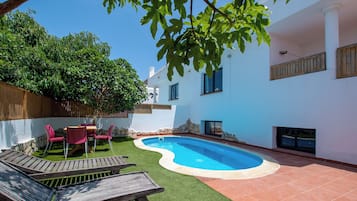 A backyard with a swimming pool, a wooden deck, and a patio area.