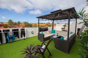 An outdoor patio with a covered seating area, artificial grass, and a row of hanging clothes.