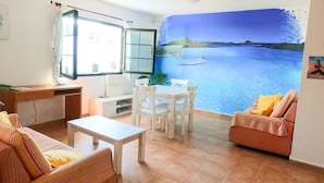 Una sala de estar con comedor, un sofá, una mesa y un cuadro de una playa.