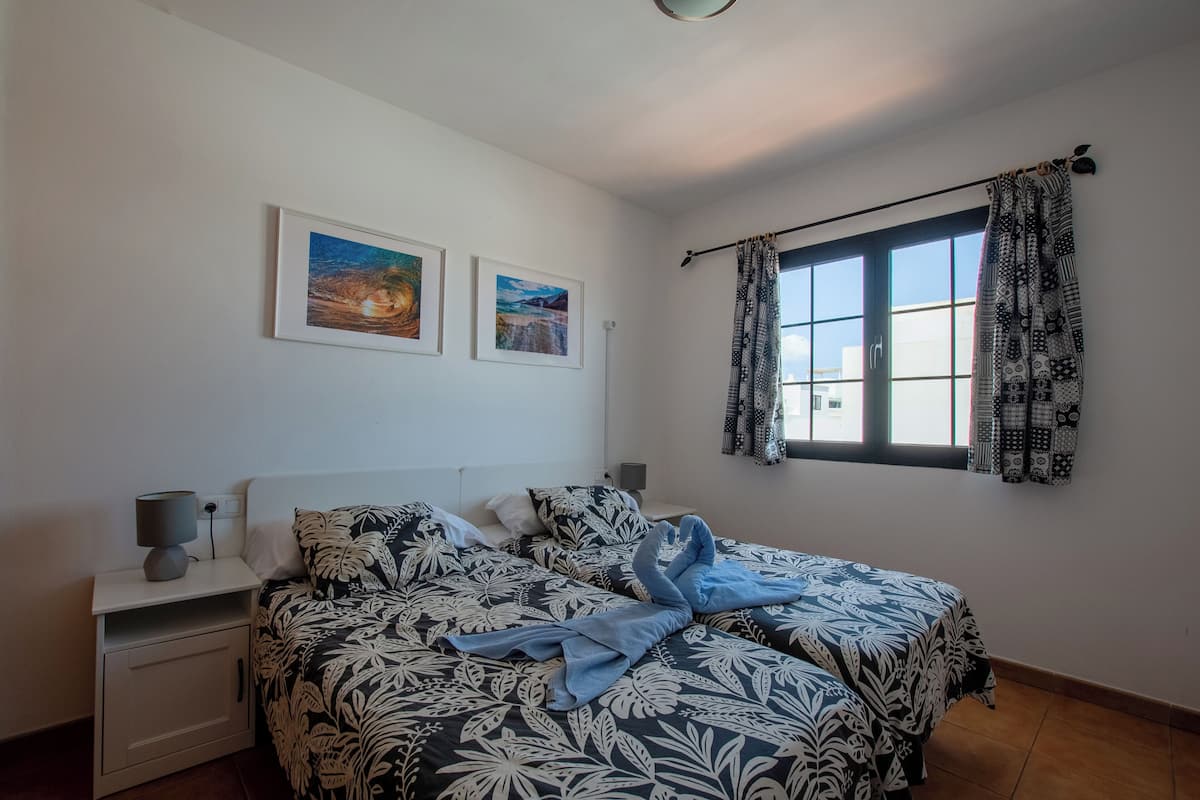 A bedroom with two beds, a nightstand with a lamp, and two framed pictures on the wall.
