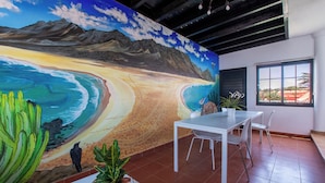 Una habitación con un mural de una playa, una mesa blanca y sillas.