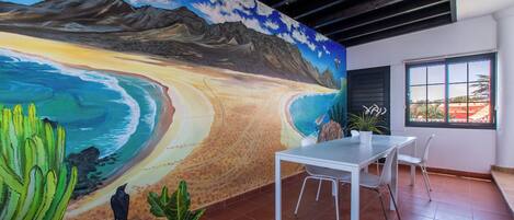 Una habitación con un mural de una playa, una mesa blanca y sillas.