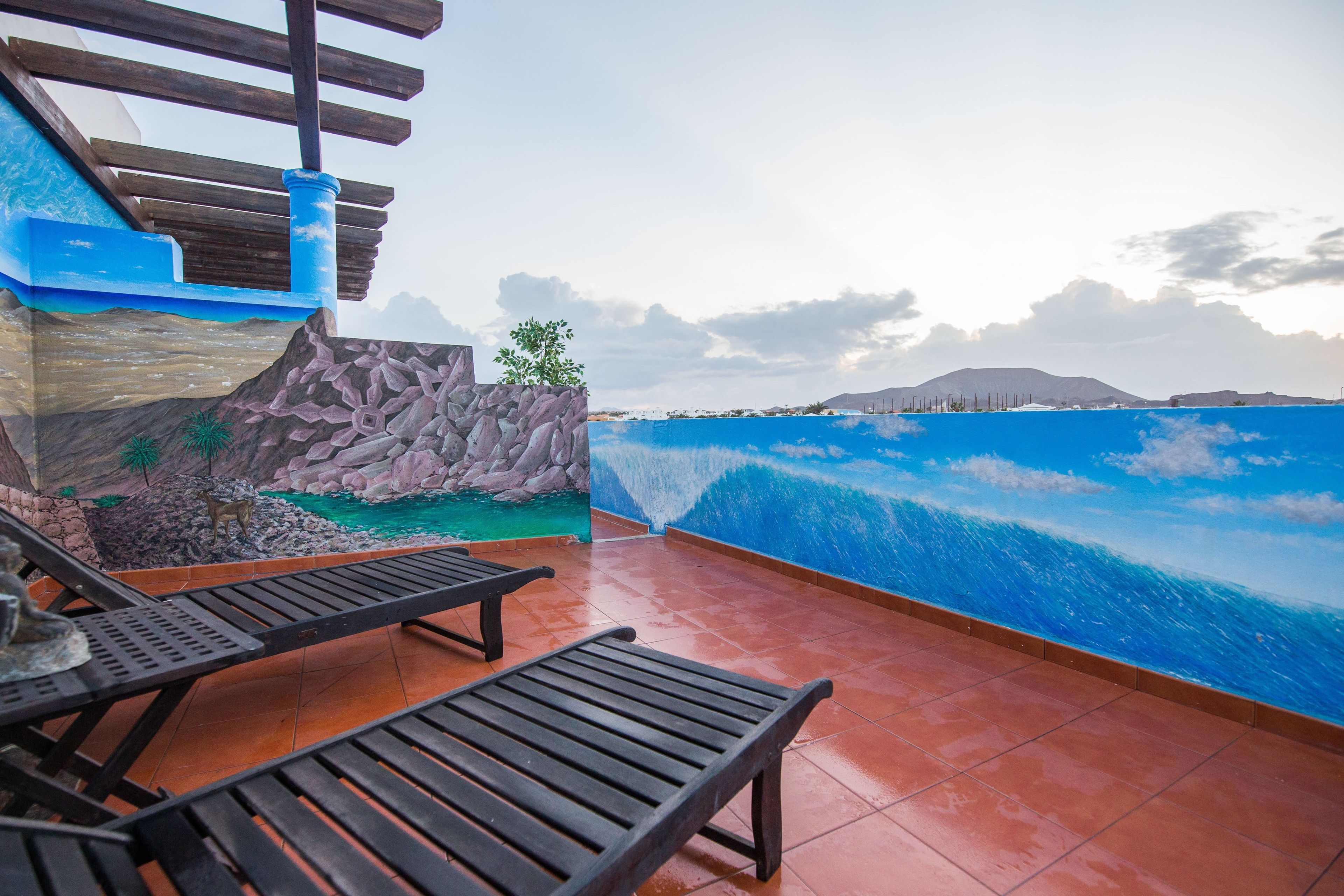 Una terraza con sillones de madera, un muro de piedra con un mural y vista al océano.