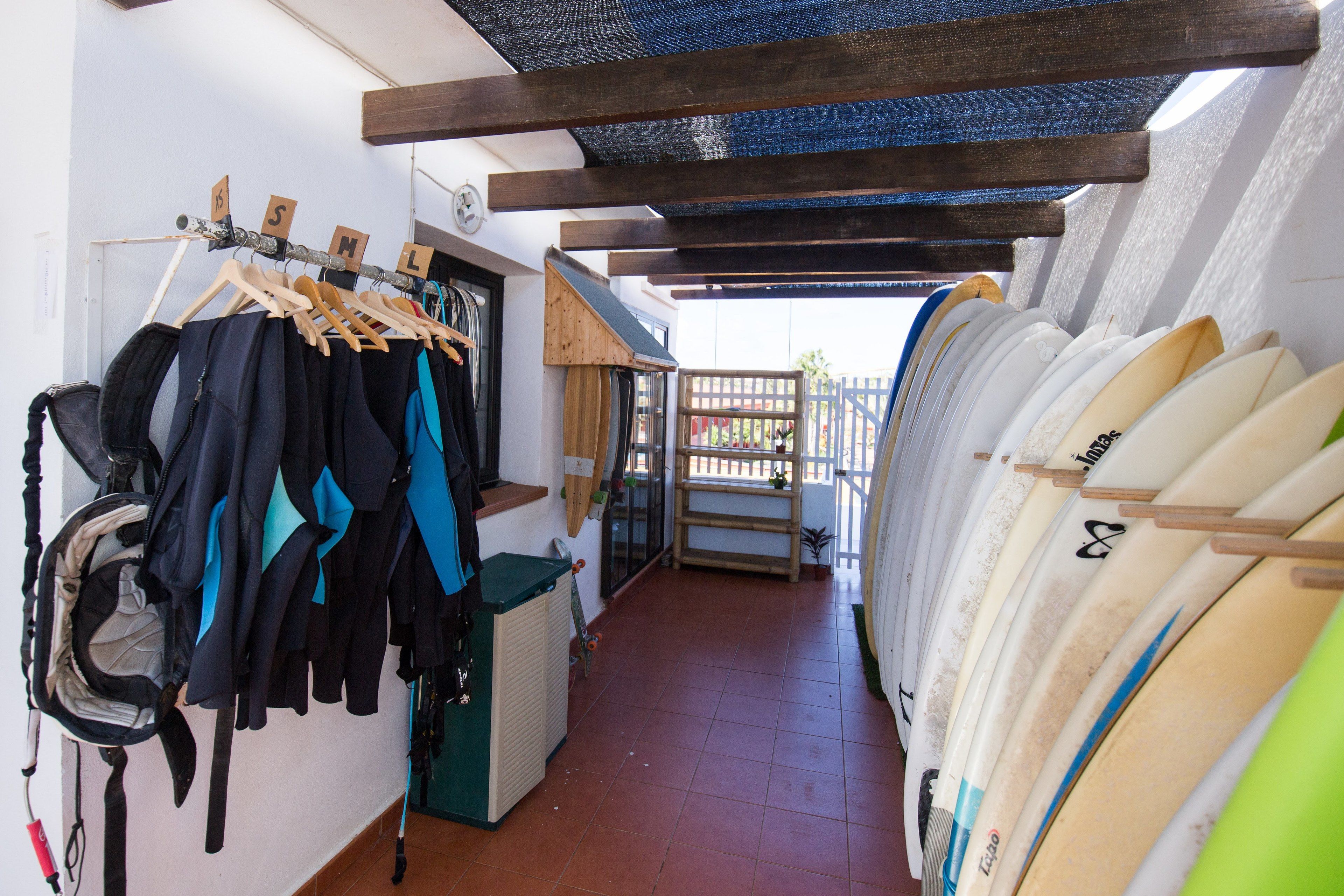 Un pasillo con tablas de surf y trajes de neopreno en estantes, que conduce a un balcón con vistas.