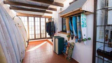Een smalle gang met surfplanken en skateboards langs de muur, een klein raam en een deur naar een andere kamer.