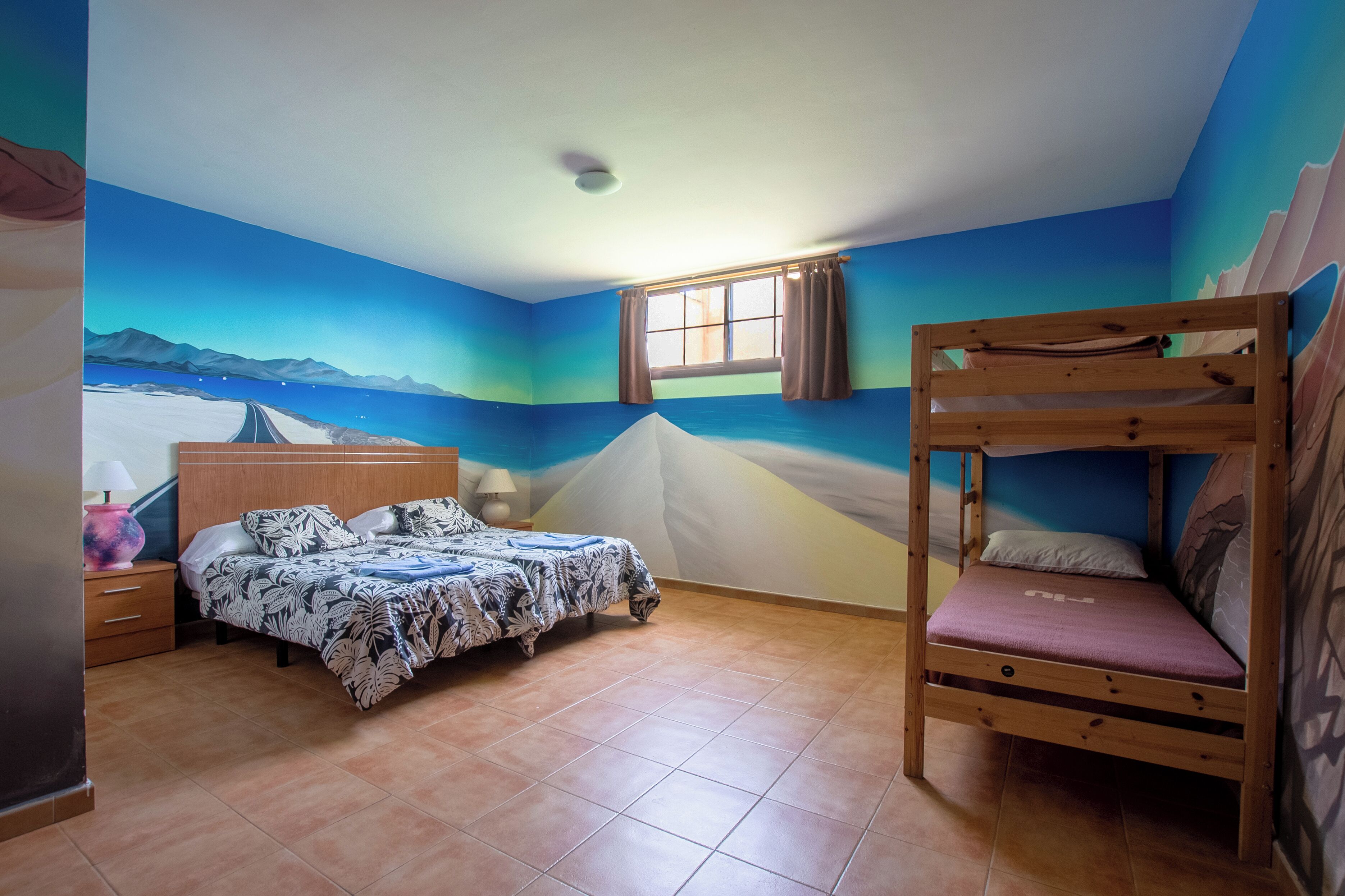Een slaapkamer met een bed, een stapelbed, een raam en een muurschildering van een landschap.
