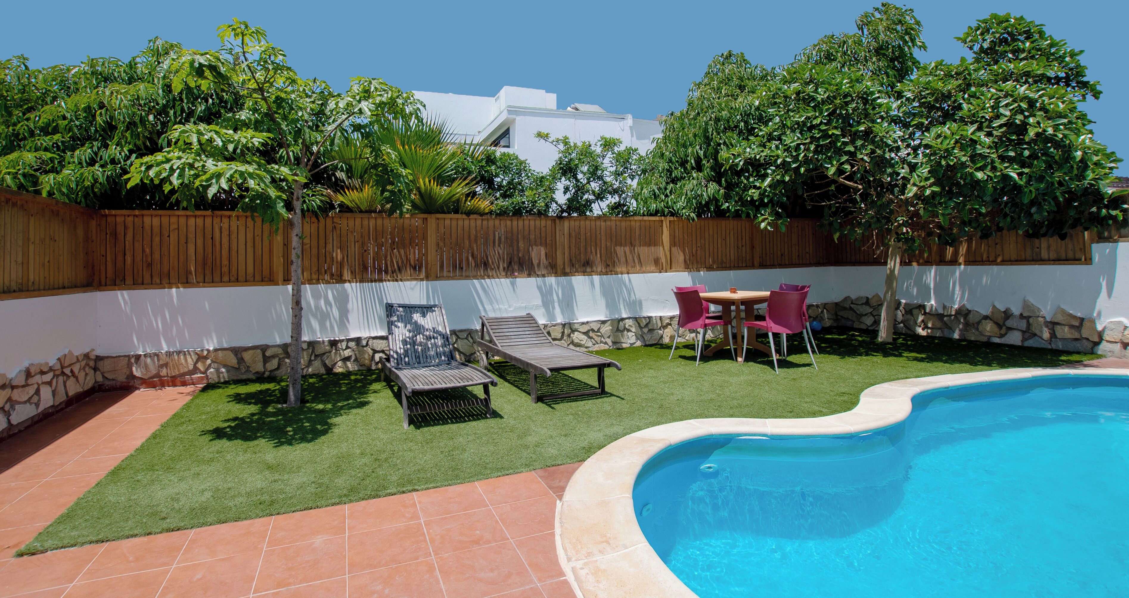 Un patio trasero con piscina, césped artificial, valla de madera y mobiliario exterior.