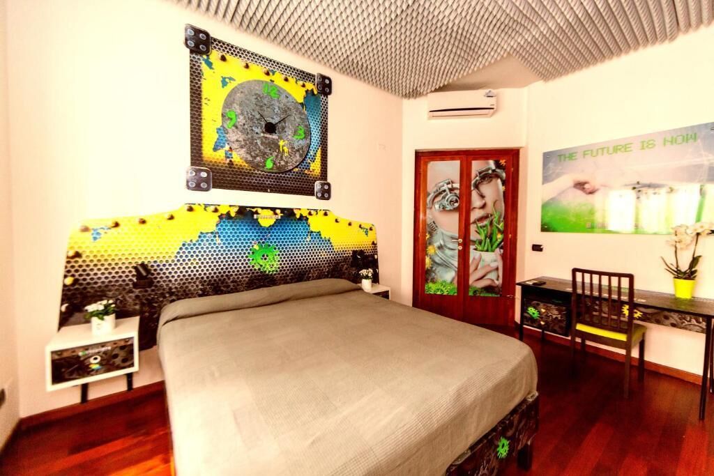 Une chambre à coucher avec un lit, une horloge murale, un bureau avec une chaise et une porte ornée d’une affiche.