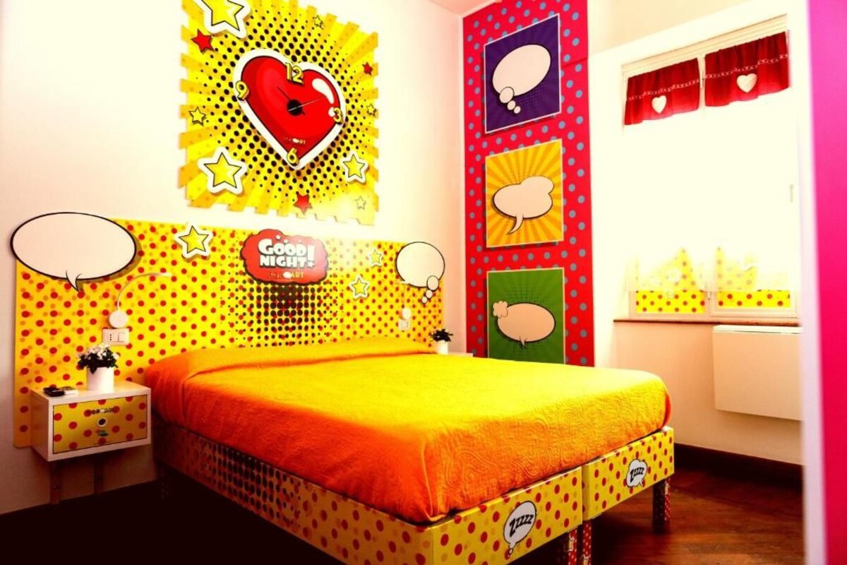 A room with a bed, a nightstand, a wall clock, and a window with curtains.