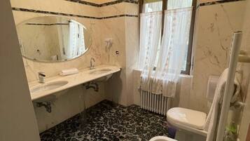 Ein Badezimmer mit zwei Waschbecken, einer Toilette, einem Bidet, einem Spiegel und einem fenster mit Vorhängen.