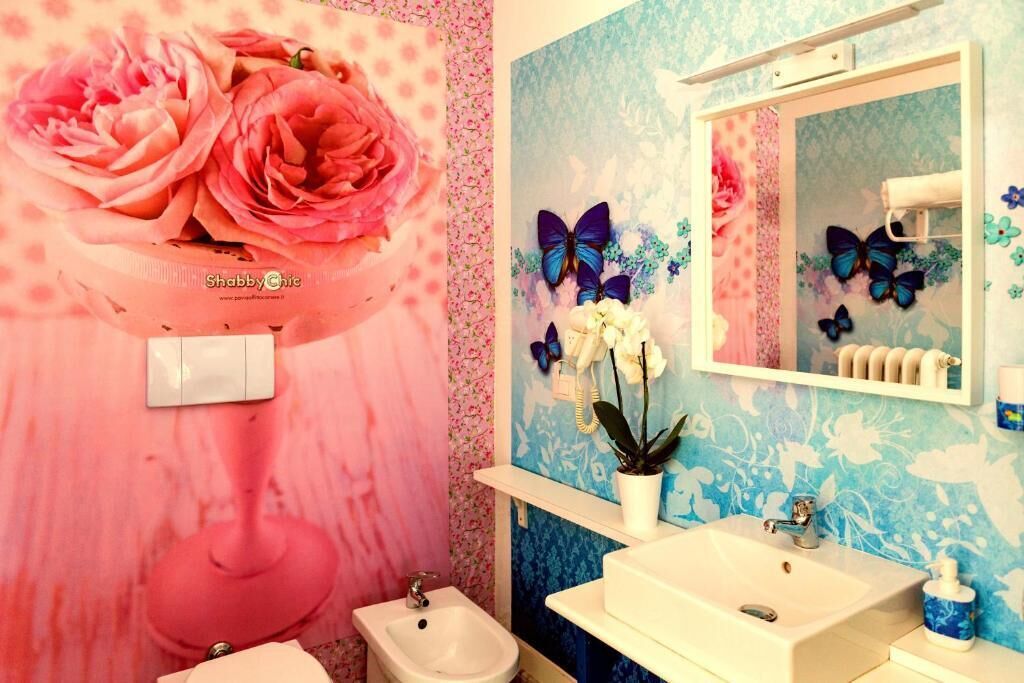 A bathroom with a pink floral wallpaper, a white sink, a mirror, and decorative butterflies.