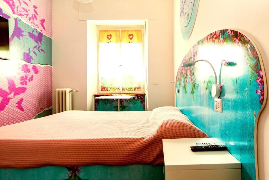 Ein Schlafzimmer mit Bett, Nachttisch, Fenster mit Vorhängen und Wand mit Blumenmuster.