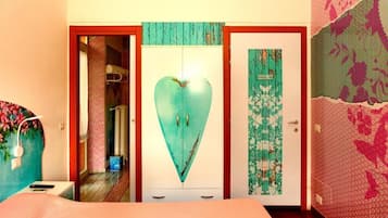 A room with a bed, a wardrobe with a heart-shaped mirror, and a door with floral wallpaper.