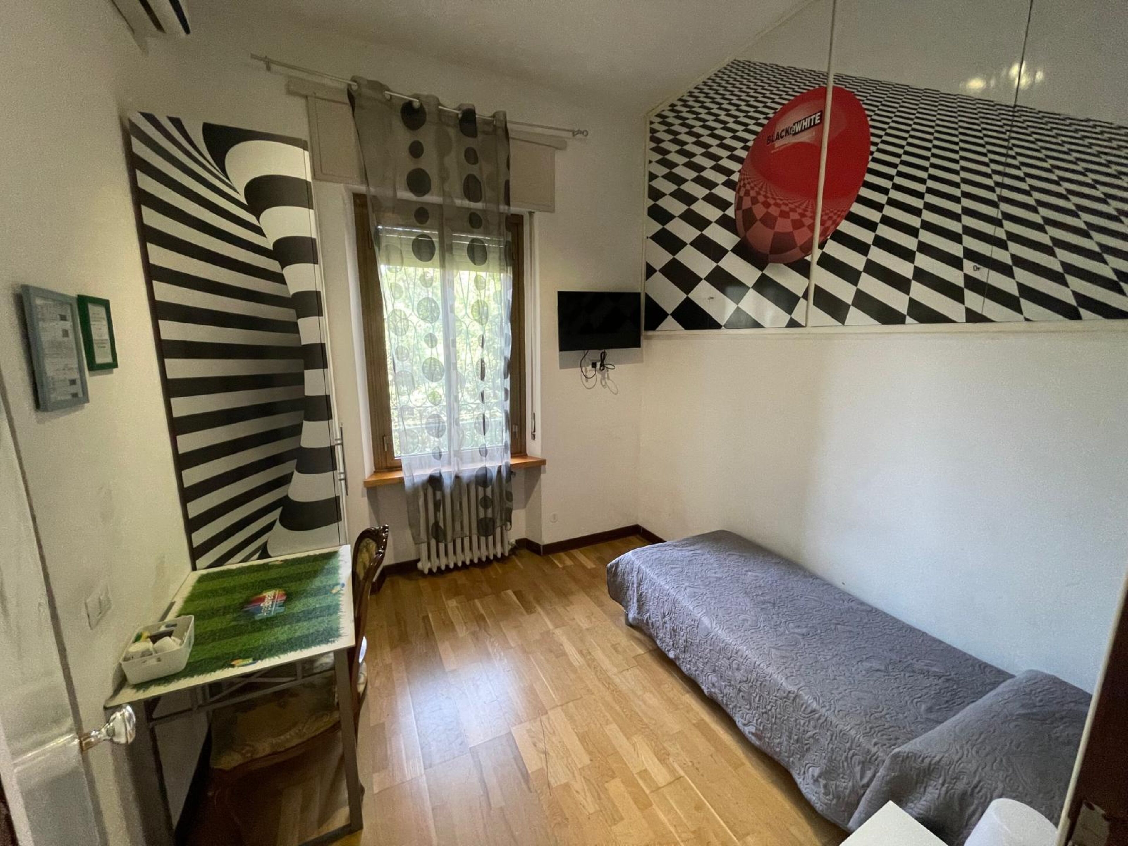 A room with a bunk bed, a small table with a green surface, a radiator, and a window with patterned curtains.
