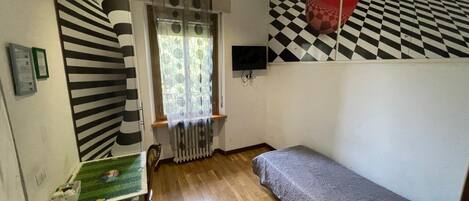 A room with a bunk bed, a small table with a green surface, a radiator, and a window with patterned curtains.